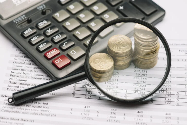 Magnifying glass over the coin stack and calculator on financial report