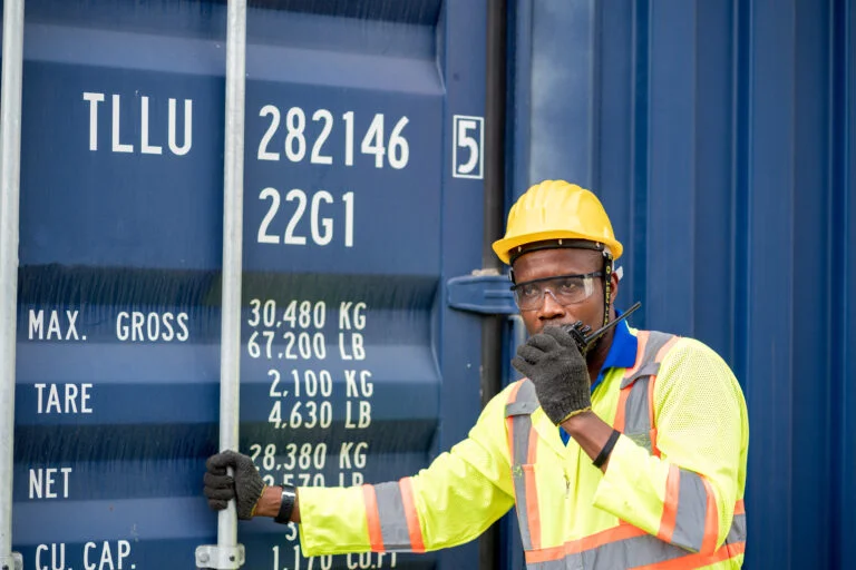 Engineer talking on walkie talkie standing by container